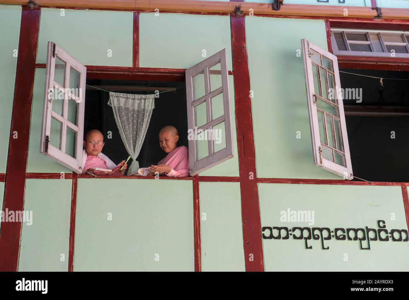 Giovani suore che guardano fuori dalla loro finestra dormitorio a Zayertheingi, un nunnery buddista a Sagaing, una città fuori Mandalay, Myanmar. Foto Stock