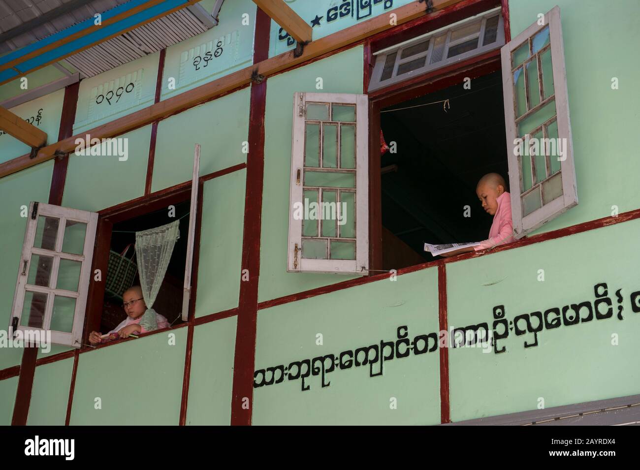 Giovani suore che guardano fuori dalla loro finestra dormitorio a Zayertheingi, un nunnery buddista a Sagaing, una città fuori Mandalay, Myanmar. Foto Stock