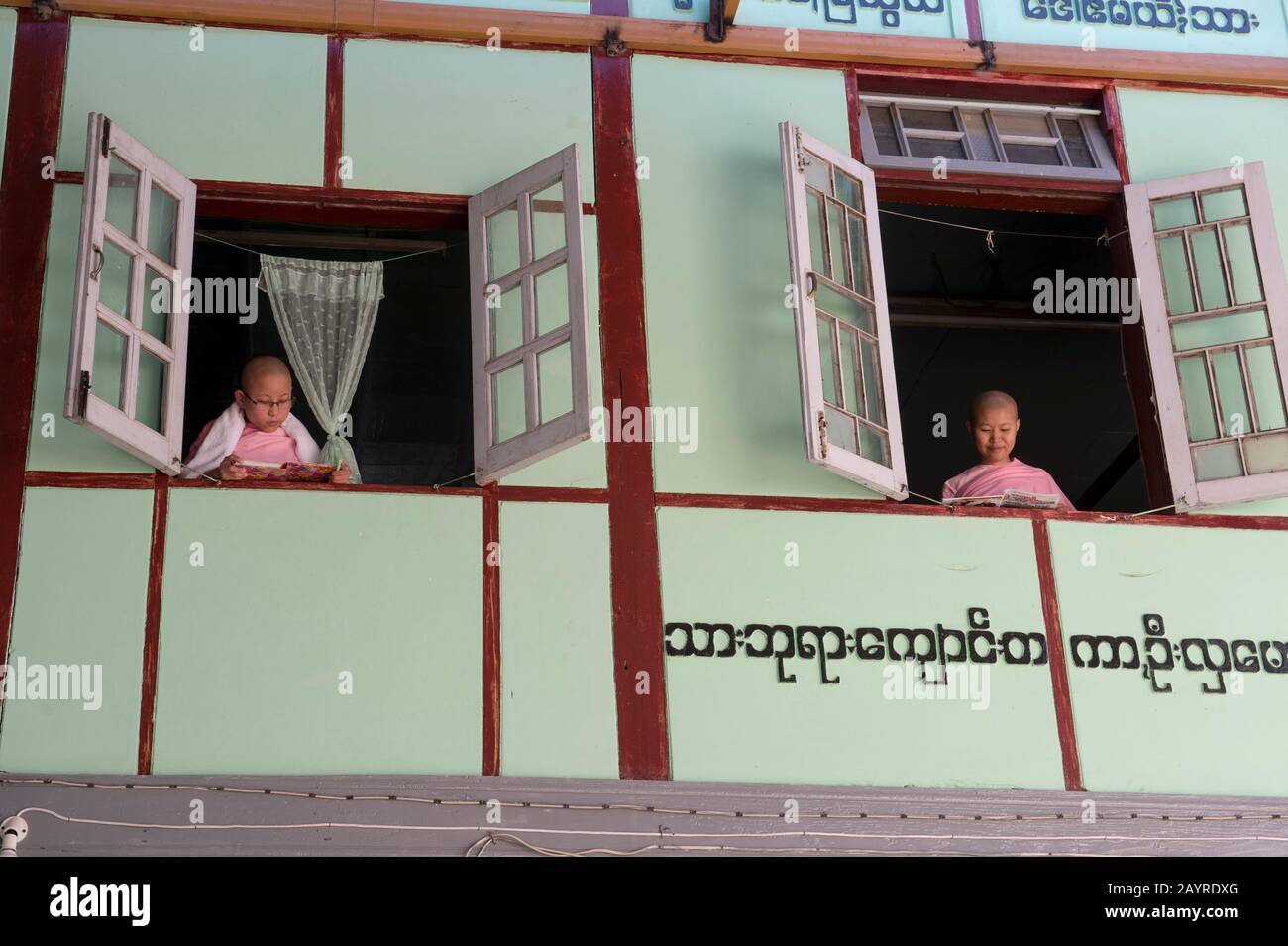 Giovani suore che guardano fuori dalla loro finestra dormitorio a Zayertheingi, un nunnery buddista a Sagaing, una città fuori Mandalay, Myanmar. Foto Stock