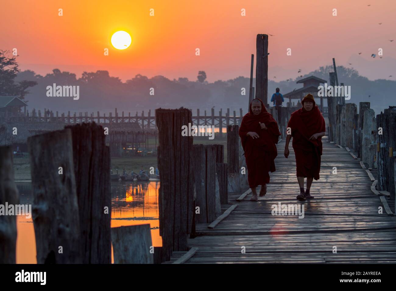 Monaci buddisti che camminano all'alba sul ponte U Bein (costruito intorno al 1850 e si ritiene che sia il più antico e più lungo ponte di legno di teak del mondo) spann Foto Stock