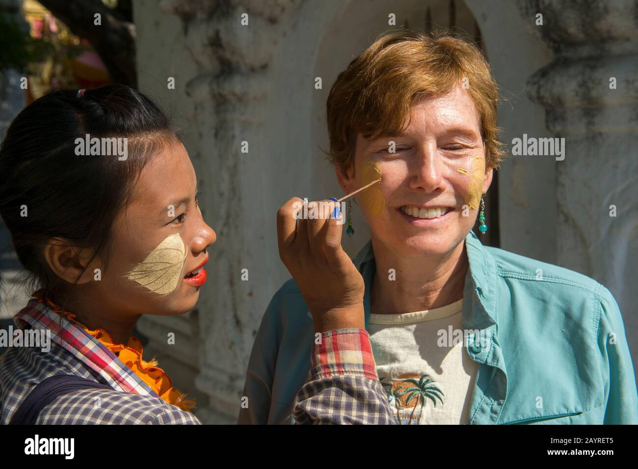 Una giovane donna sta mettendo la pasta fatta dall'albero di Thanaka su una faccia di un turista alla Pagoda di Kutodaw sulla collina di Mandalay, Mandalay, Myanmar. Foto Stock