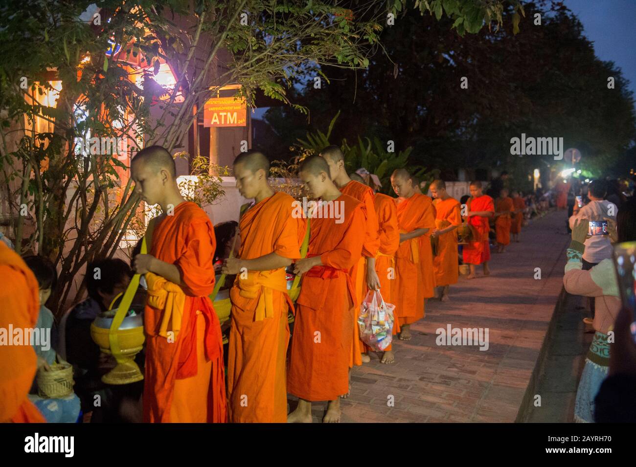 Monaci buddisti che ricevono elemosina dalla gente la mattina presto prima dell'alba nella città patrimonio dell'umanità dell'UNESCO di Luang Prabang nel Laos centrale. Foto Stock