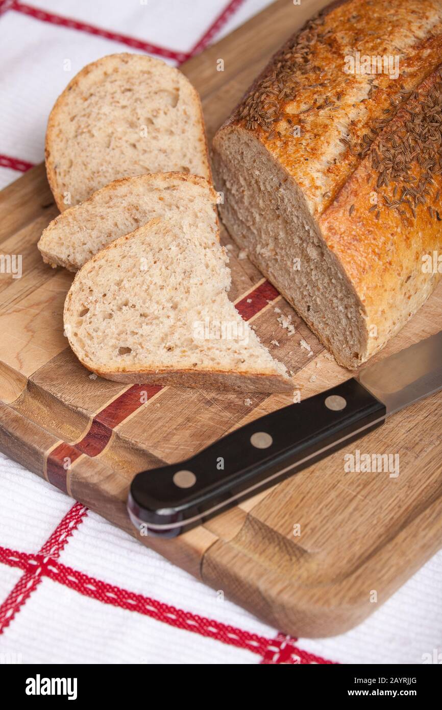 Pane di segale macinato di pietra con fette, su un tagliere di legno su un tovagliolo da tè, con un coltello da pane Foto Stock