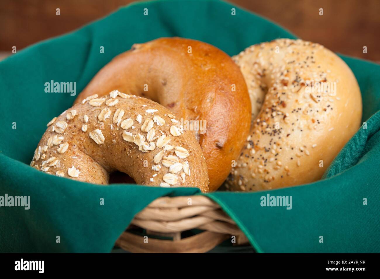 Tre varietà di bagel (grano intero, cannella swirl e raisen, e tutto) che riposano in un cesto di pane rivestito di tovagliolo Foto Stock