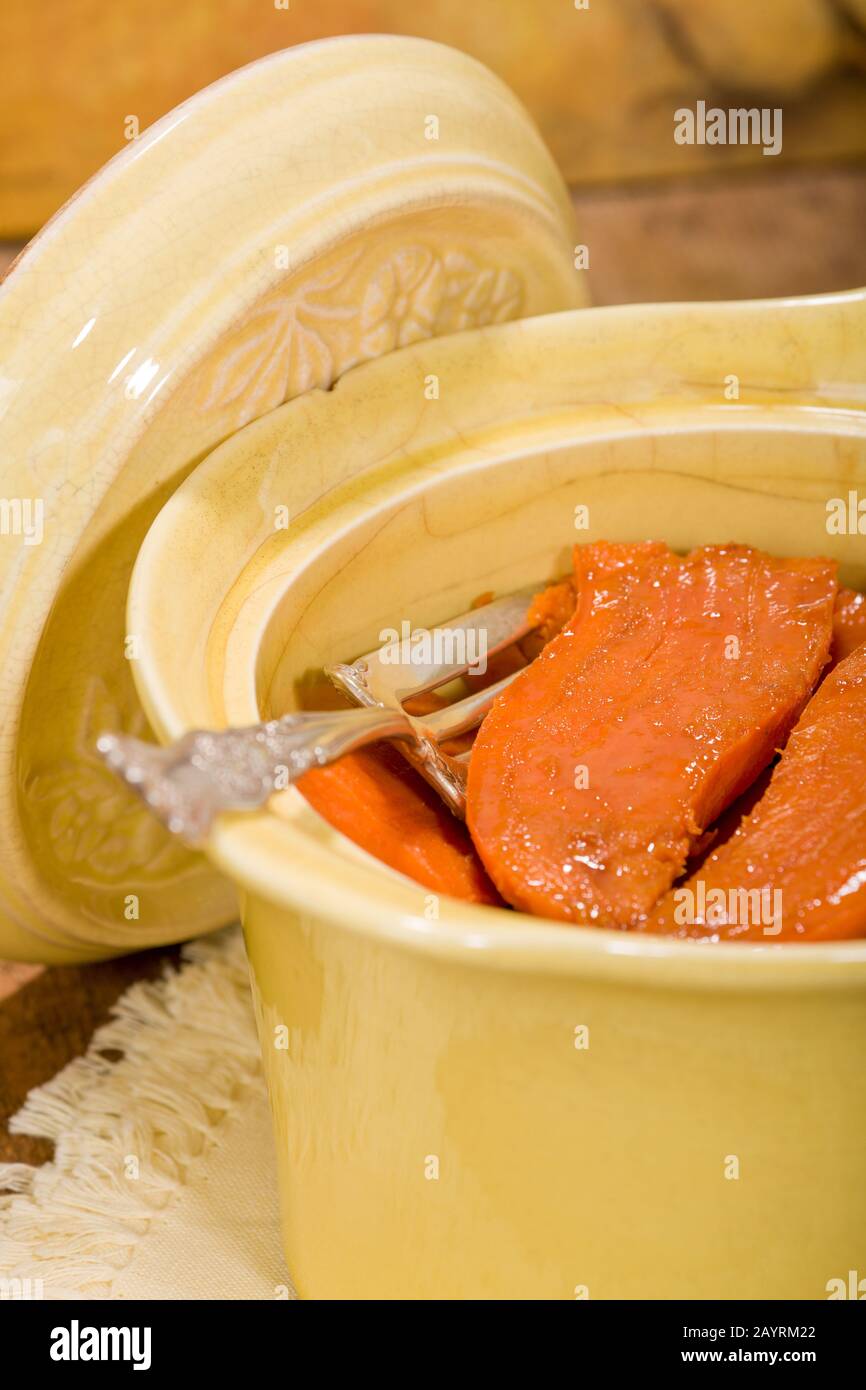Patate dolci candite al forno in una casseruola rotonda antica che riposa su un tovagliolo di stoffa, su un tavolo rustico in legno Foto Stock