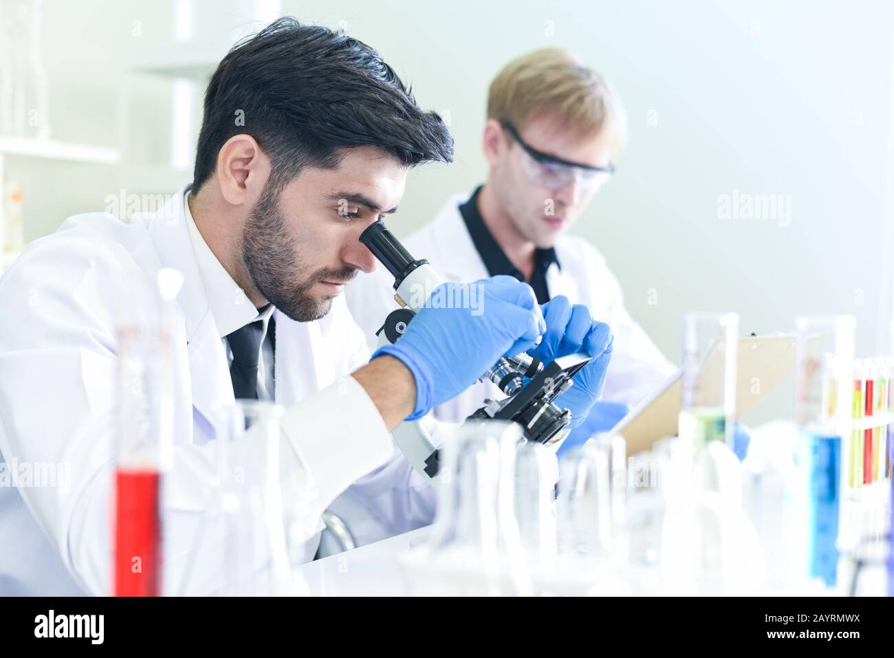 Team di ricerca scientifica lavorando insieme condurre esperimenti e guarda al microscopio in moderno laboratorio / Scienziati in laboratorio biochimica genetica Foto Stock
