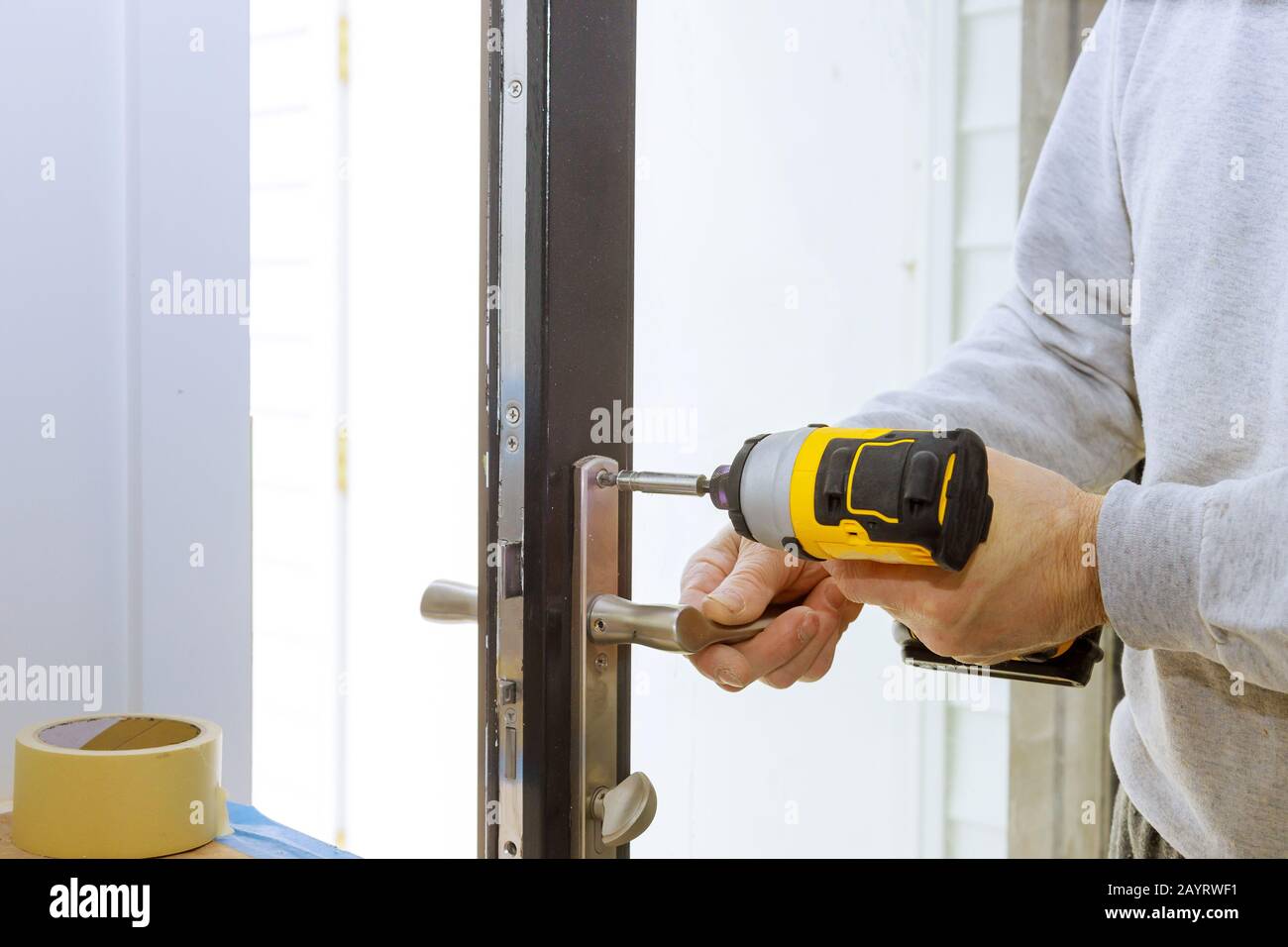 Installare la maniglia della porta con una serratura, falegname serrare la vite utilizzando un trapano elettrico cacciavite, close-up. Foto Stock