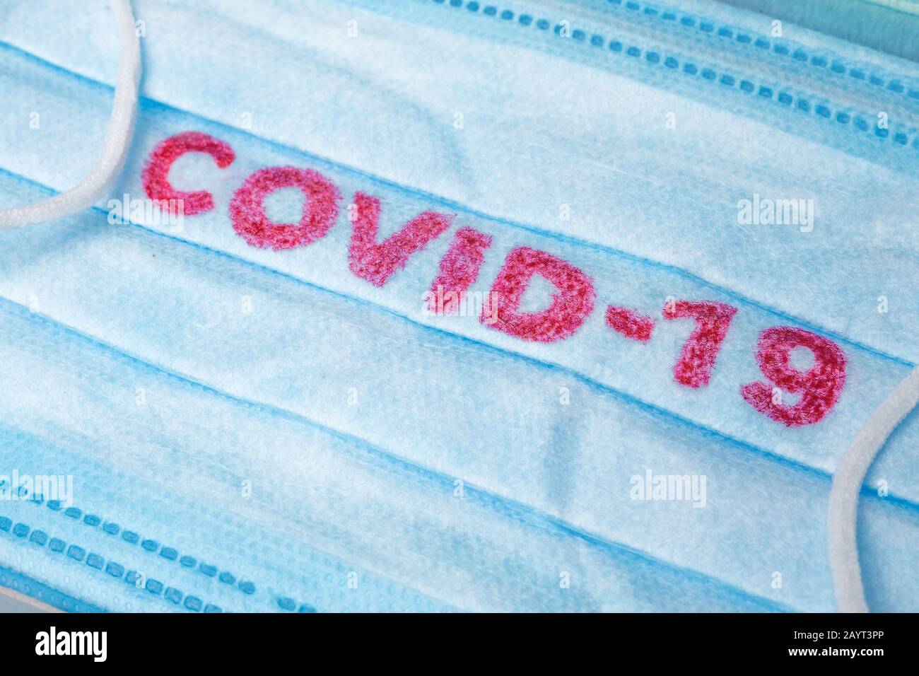 Covid-19 - Il Romanzo di Wuhan Coronavirus polmonite ottiene il nome ufficiale DA CHI: COVID-19. Medicazione monouso sul viso. Contesto sanitario. Maschera facciale monouso per uso medico blu con stampa covid-19 Foto Stock