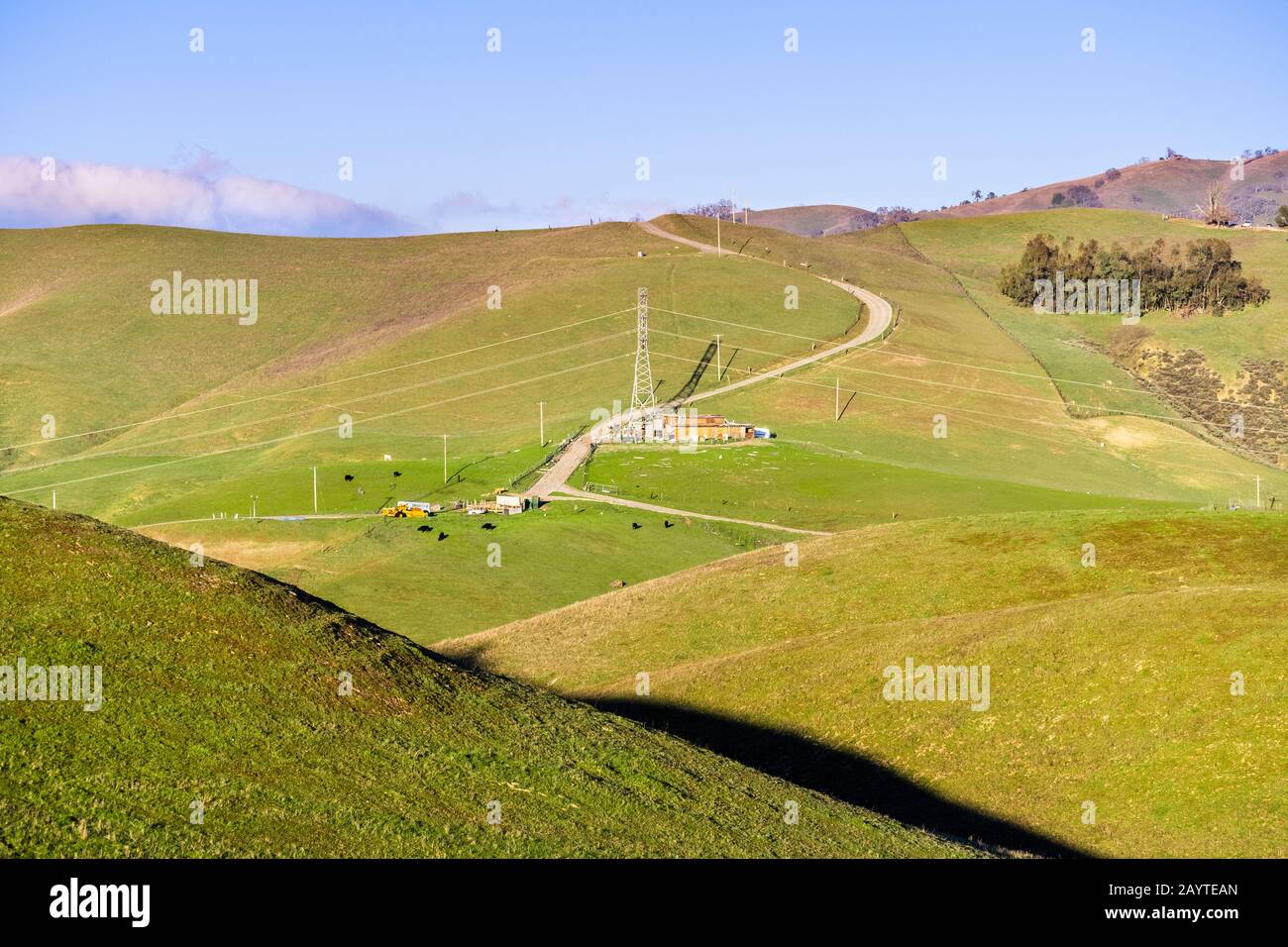 Torre elettrica ad alta tensione e granaio circondato da verdi colline e valli nella catena montuosa Diablo Range nell'area della Baia di San Francisco Sud; San Foto Stock