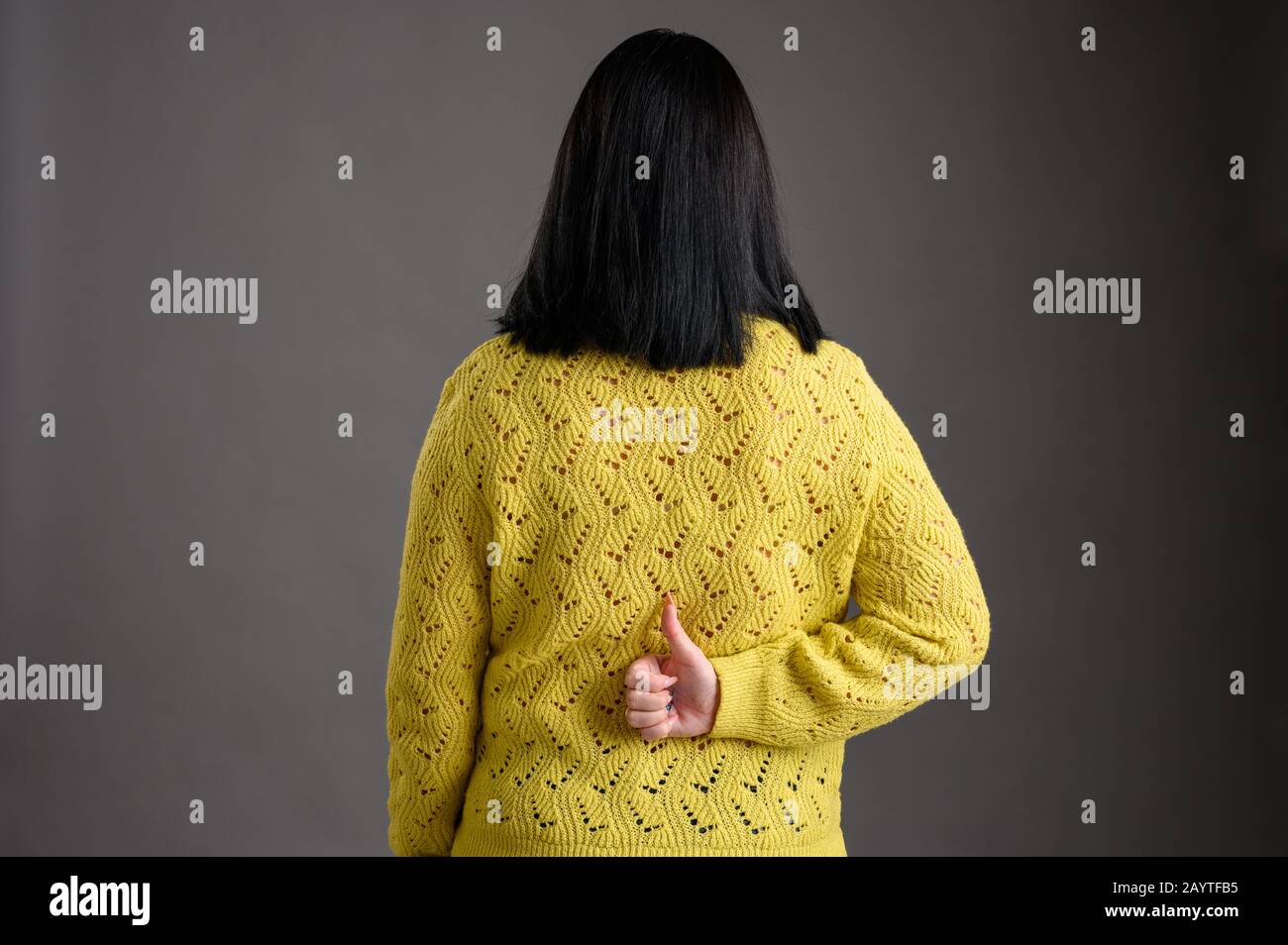 Giovane donna con i capelli neri che si posano vestiti in un maglione giallo che mostra i tuoni dietro la sua isolata su sfondo grigio Foto Stock