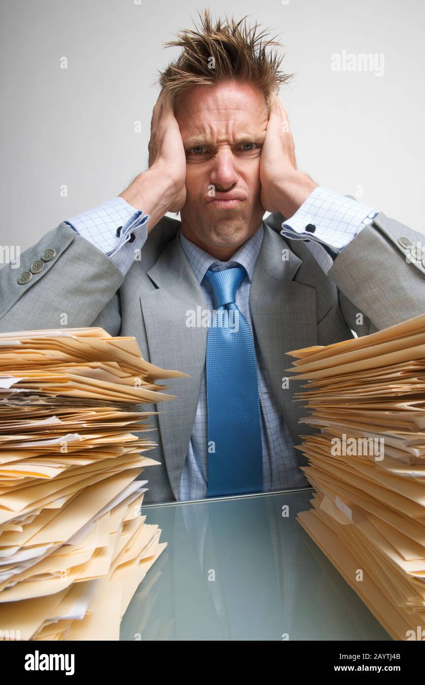 Un lavoratore in ufficio frustrato si è bloccato sulle grandi pile di cartelle di file sulla sua scrivania Foto Stock
