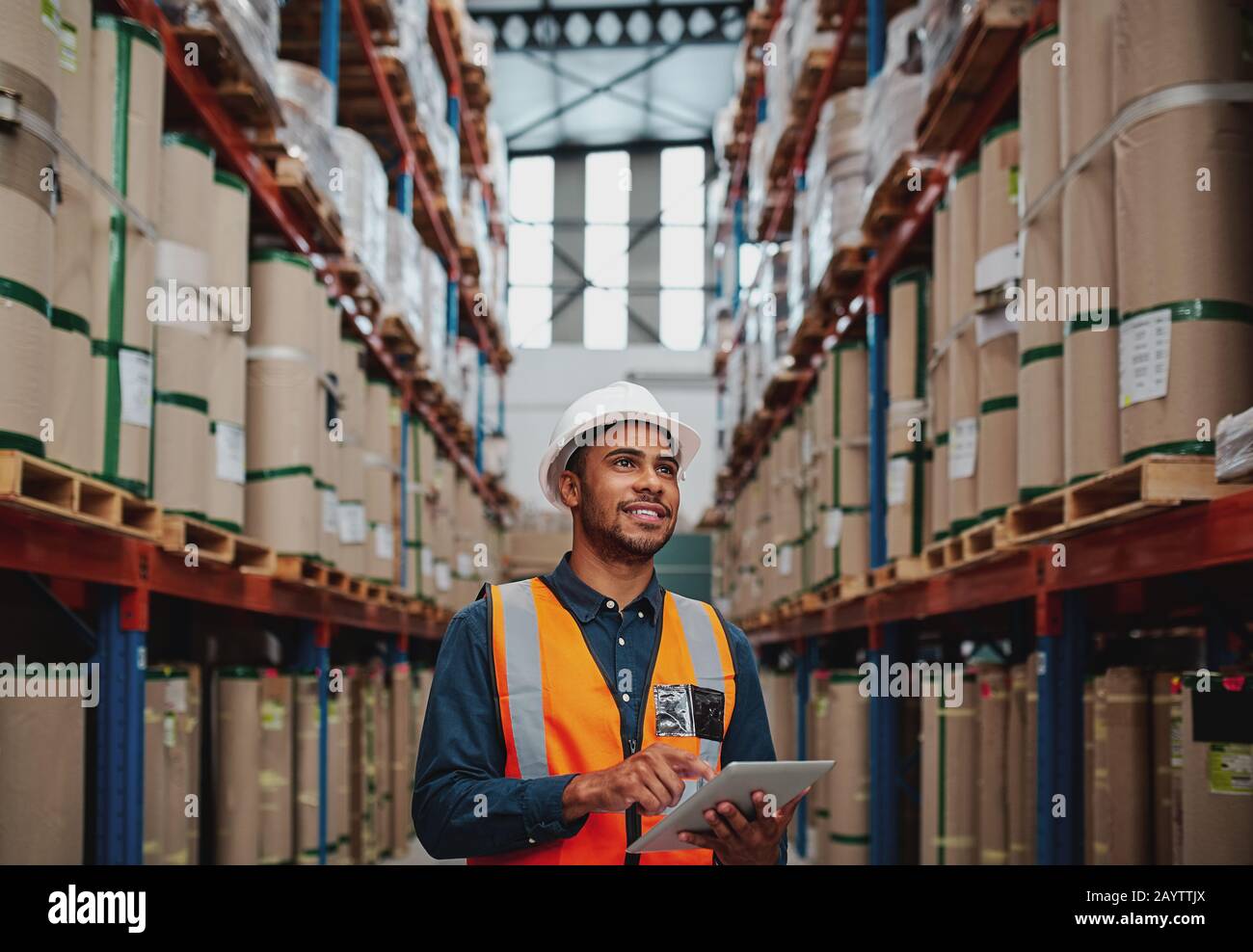 Il lavoratore di magazzino bello usa il tablet digitale per controllare le scorte, sulle scatole di cartone verticali degli scaffali Foto Stock