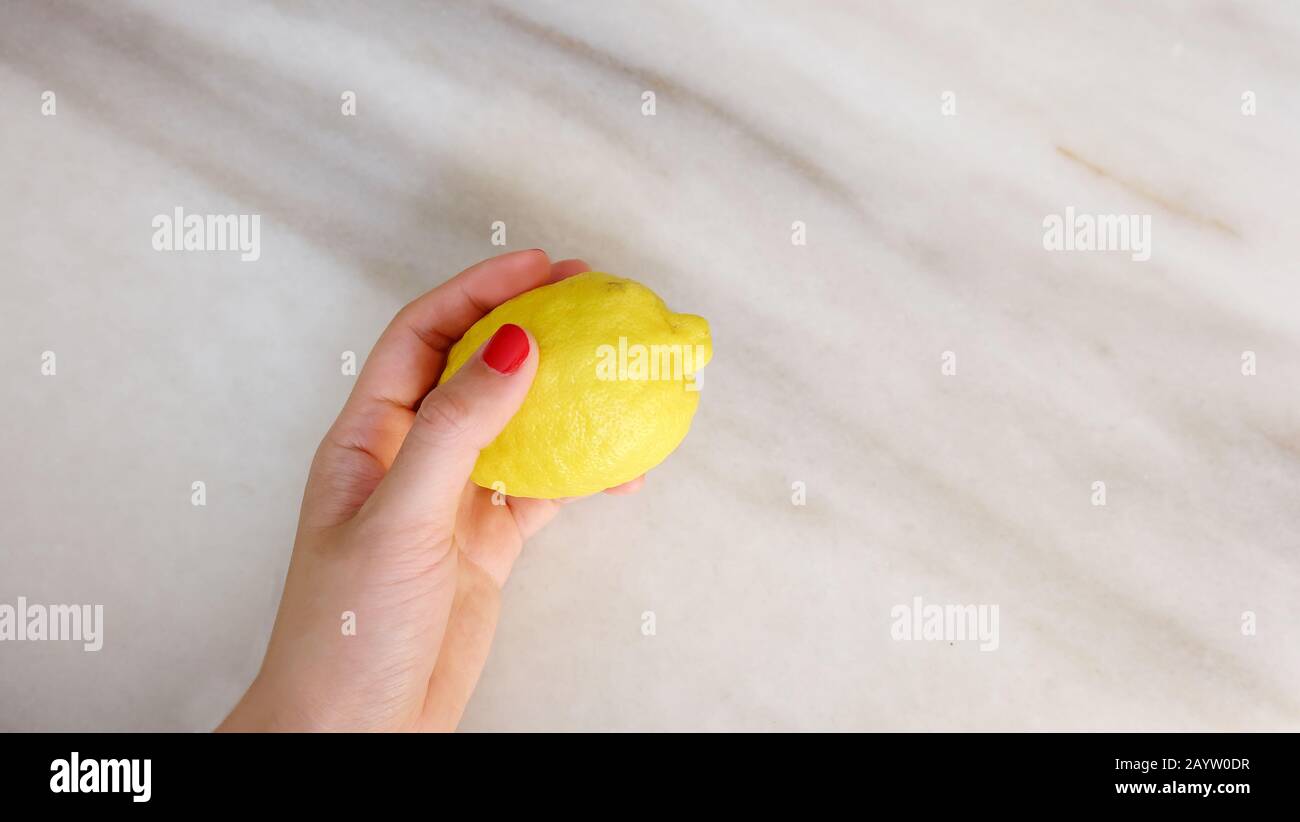 Una mano con vernice rossa per unghie, contenente un limone giallo. Foto Stock