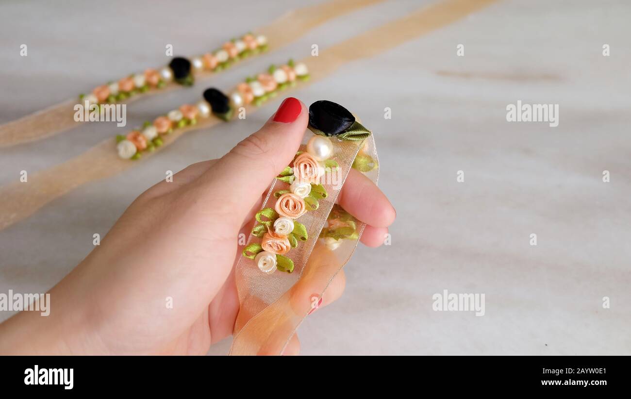 Una mano che tiene un corsalvia di fiore fatto con i fiori del nastro e le perle false, con due corsates più simili nello sfondo. Foto Stock