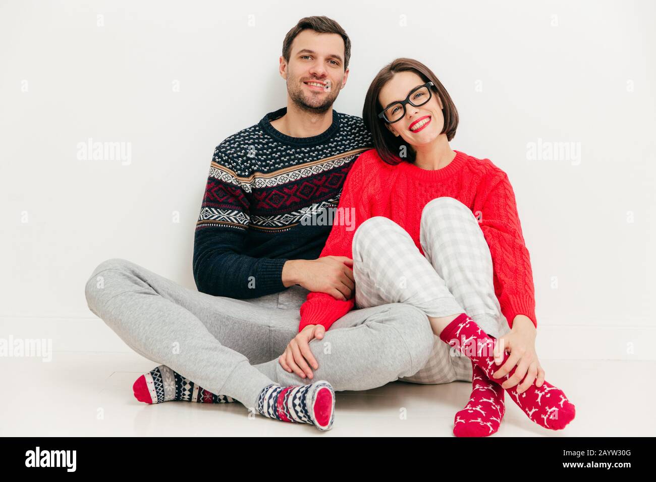 Inquadratura orizzontale di felici gli amanti siedono insieme contro il bianco di sfondo per studio, indossare abiti casual, godere del tempo libero a casa. Adorabili giovane femmina di un Foto Stock