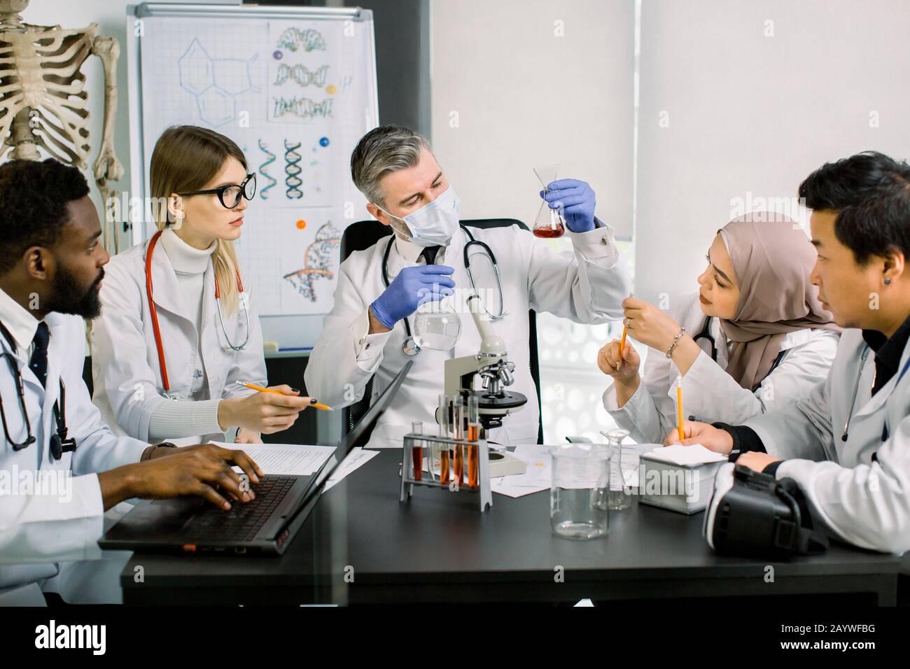 Team di scienziati multietnici in camici di laboratorio moderni condurre ricerche mediche alla ricerca di vaccini o nuovi farmaci. Uomo maturo nella maschera che guarda Foto Stock