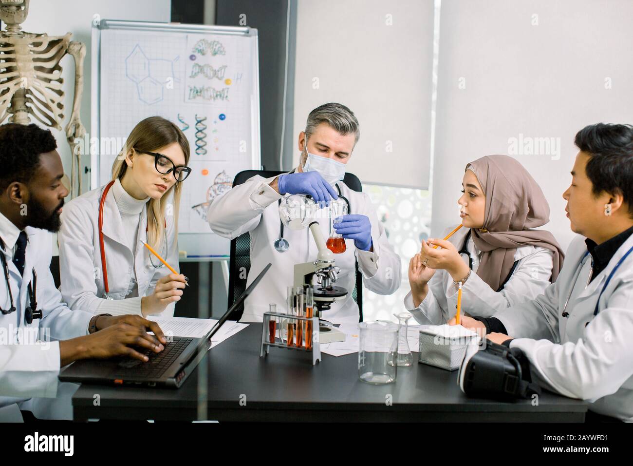 Cinque giovani medici multietnici scienziati, bioenegeri, chimici, che lavorano nel moderno centro di laboratorio. Lo scienziato maschio tiene il pallone con il campione di nuovo Foto Stock