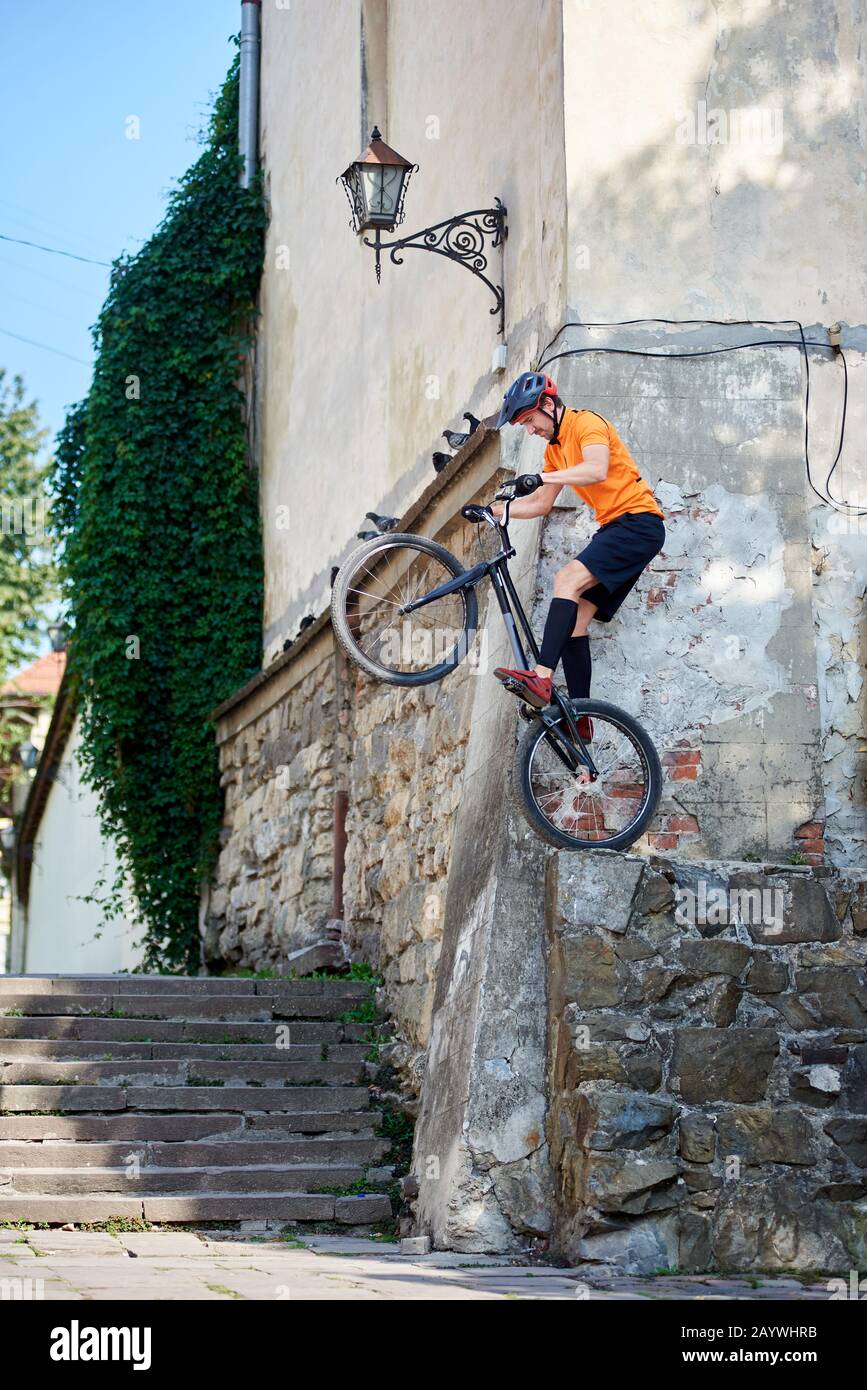 Un'istantanea laterale di un stuntman che si prepara a saltare con la sua mountain bike dall'angolo dell'antico edificio Foto Stock