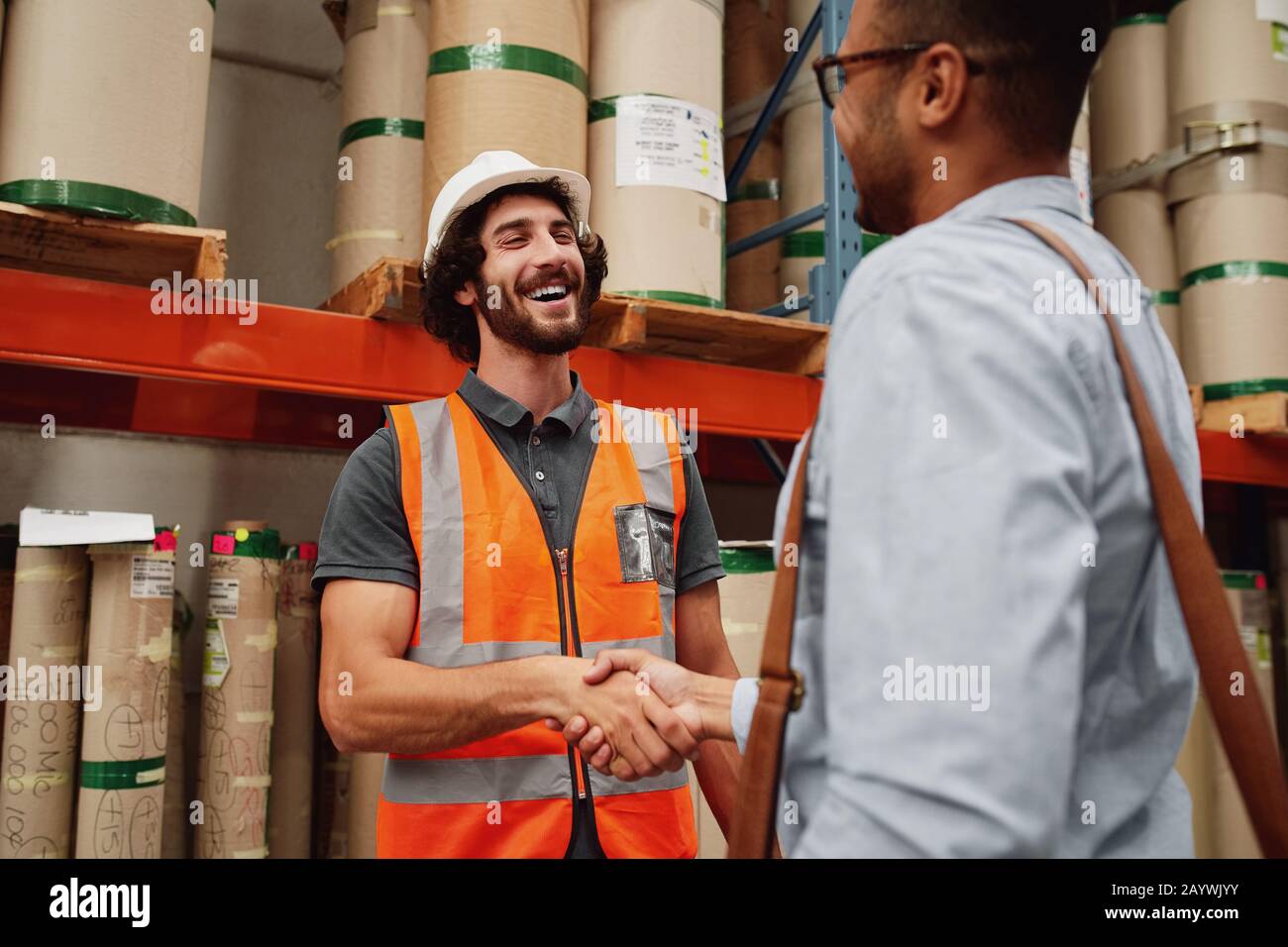 Sorridente responsabile magazzino in uniforme giacca arancione e casco saluto business partner e scuotendo le mani Foto Stock