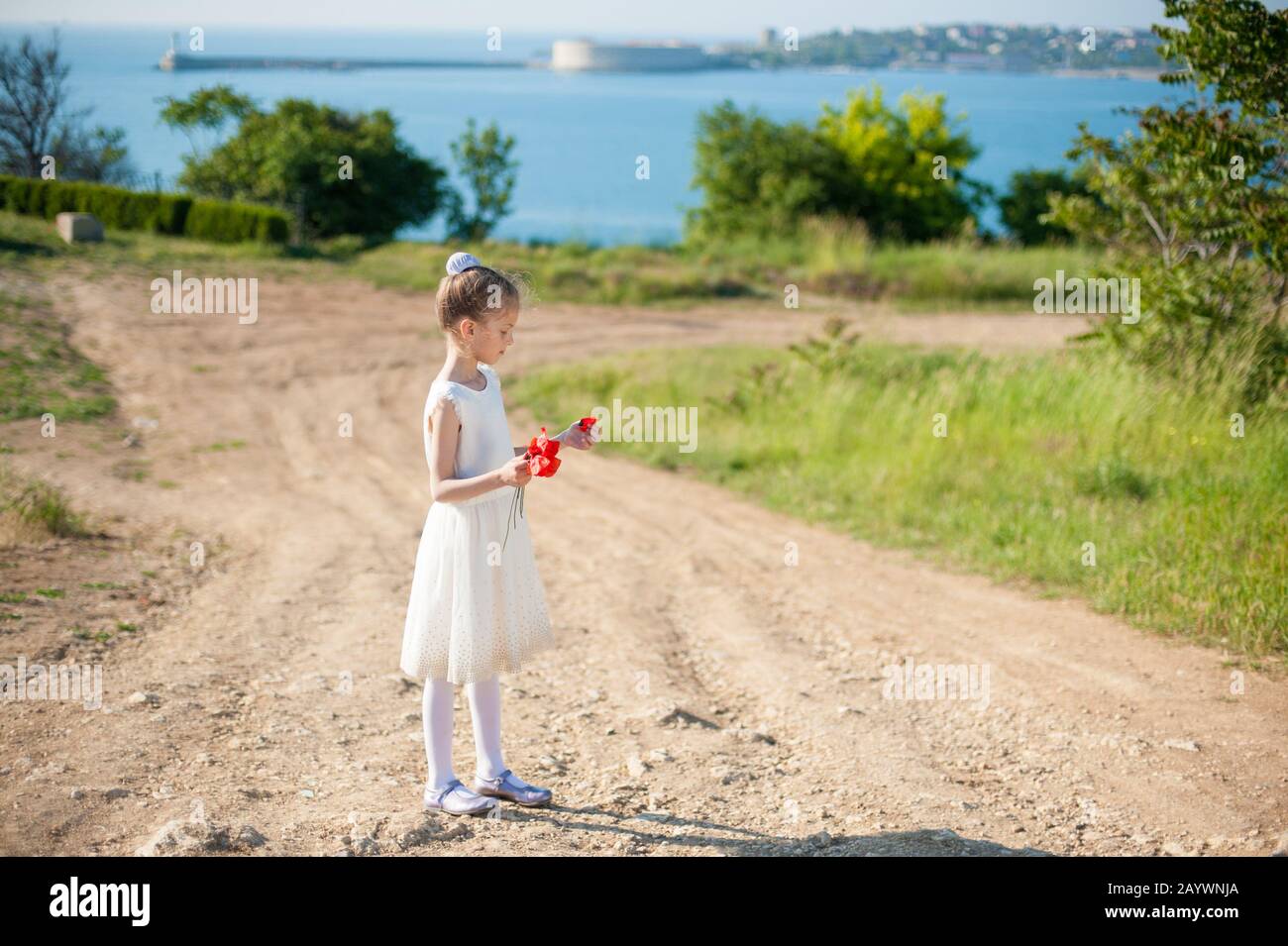 bella bambina in abito bianco che tiene papaveri rossi sullo sfondo del porto di mare Foto Stock