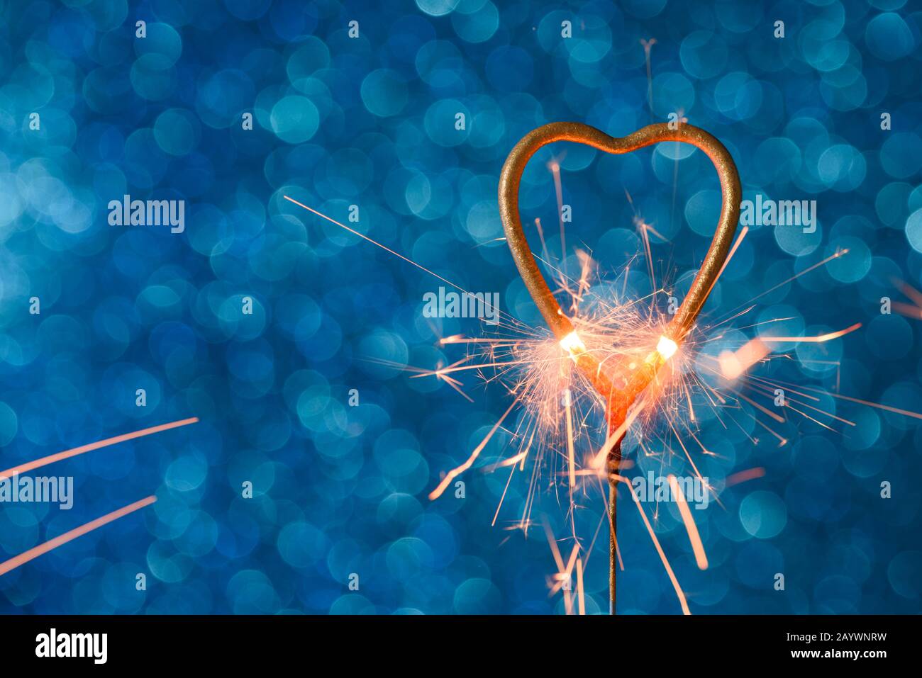 Sparkler in una forma di calore dorato che brucia su sfondo blu bokeh con copia-spazio. Matrimonio o concetto di carta d'invito di San Valentino. Foto Stock