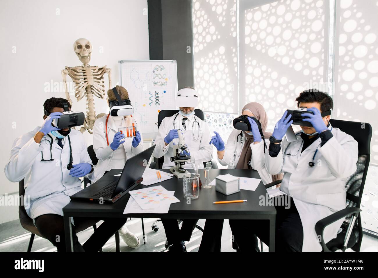 Team di farmacologi multietnici che indossano camici bianchi protettivi, guanti e occhiali di protezione vr, lavorando insieme su nuovi vaccini o farmaci in moderno Foto Stock