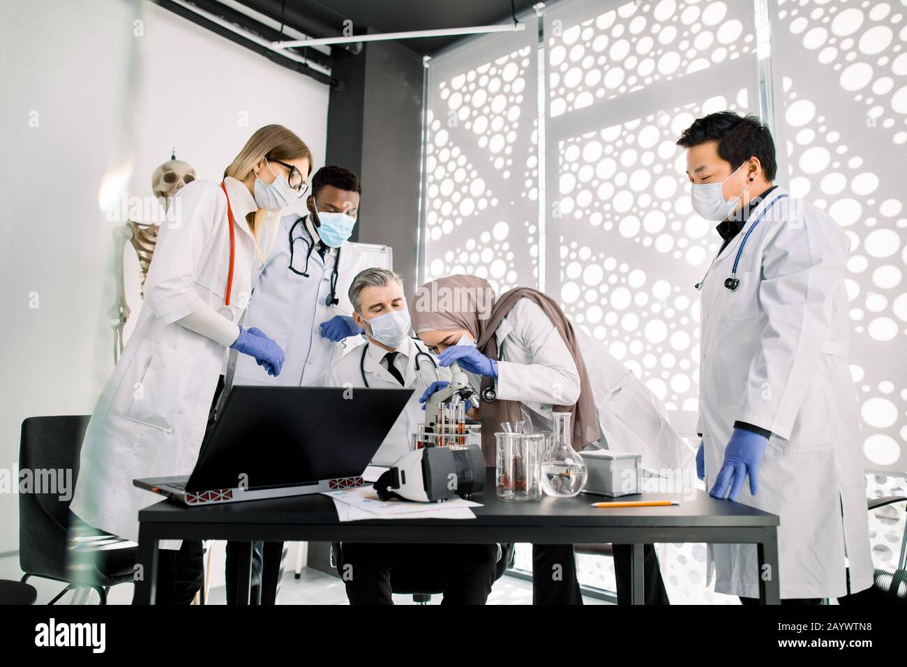 Team di scienziati medici biochimici che lavorano con il microscopio, facendo ricerche scientifiche esperimenti in laboratorio. La donna musulmana sta guardando attraverso Foto Stock