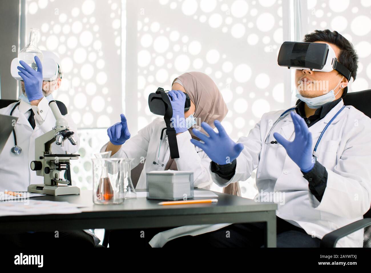 Squadra di scienziati, uomini asiatici e caucasici, donna musulmana che usa occhiali di realtà virtuale per la ricerca scientifica in laboratorio, gesturing mani Foto Stock