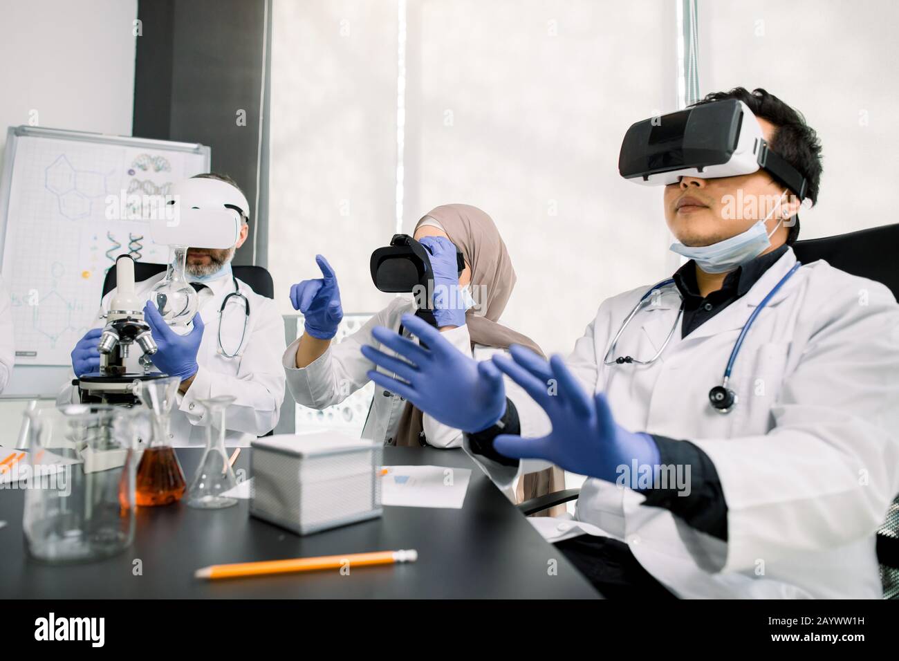 Squadra di scienziati, uomini asiatici e caucasici, donna araba che usa occhiali di realtà virtuale per la ricerca scientifica in laboratorio, gesturing mani Foto Stock