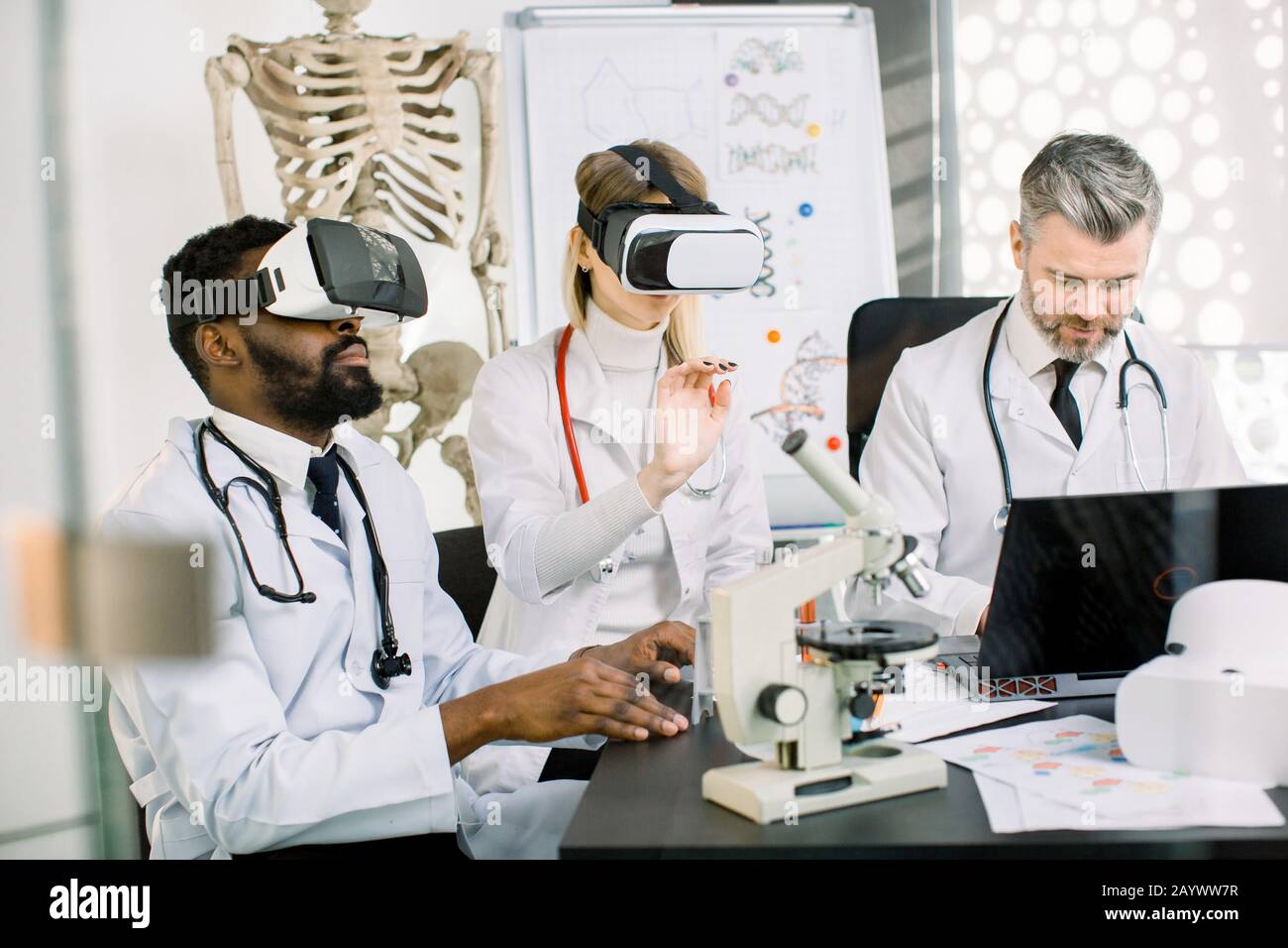 Gruppo di scienziati multietnici, uomo africano, donna caucasica e uomo, utilizzando occhiali di realtà virtuale per la ricerca in laboratorio. Sviluppo di nuovi Foto Stock