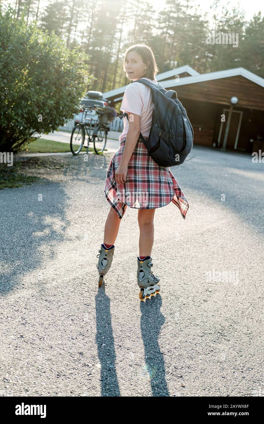 Donna caucasica con zaino urbano pattinaggio a rotelle in una soleggiata giornata estiva. Vacanze attive. Foto Stock