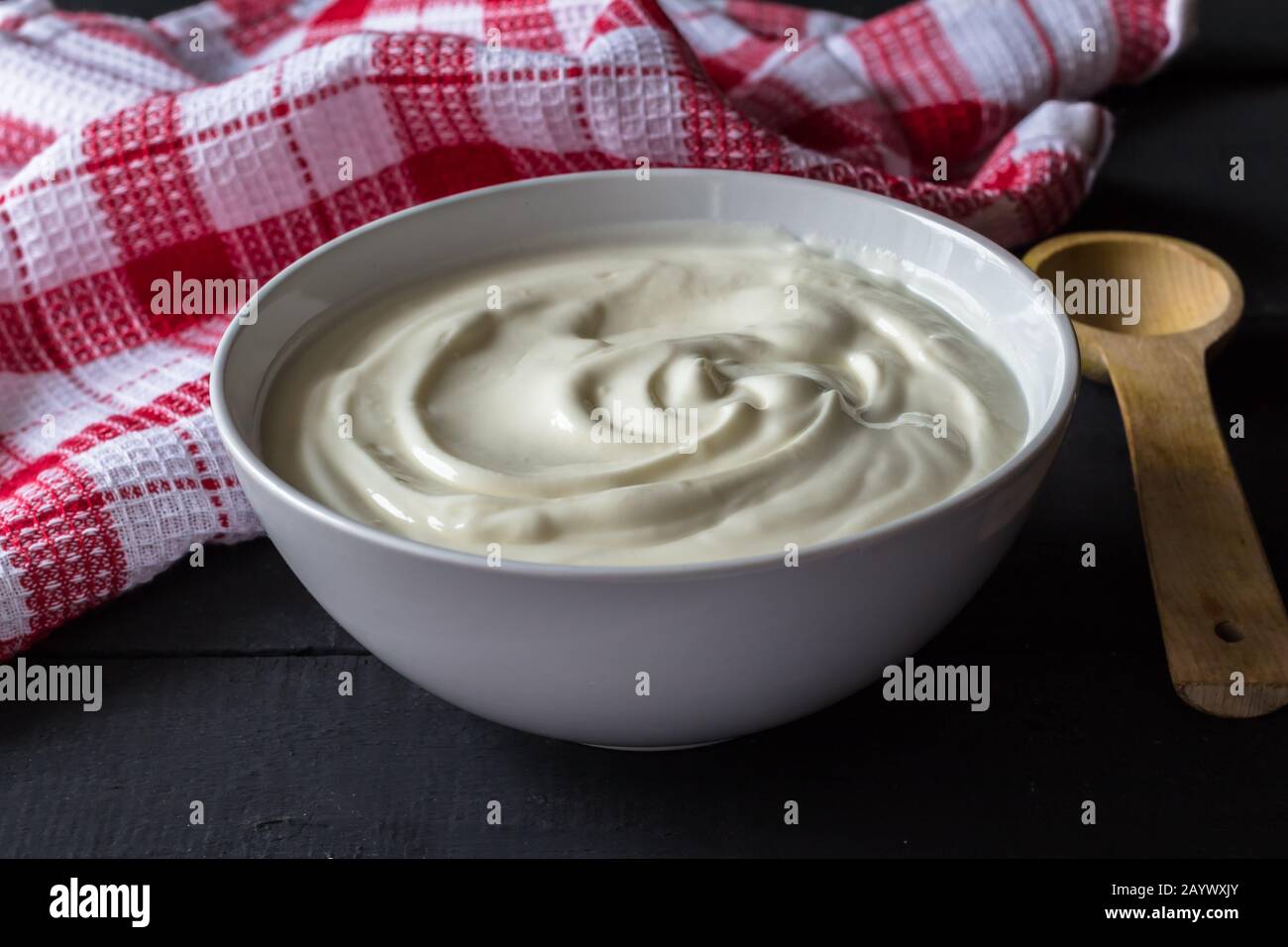 Yogurt in una ciotola bianca su un rustico tavolo di legno nero con cucchiaio di legno - yogurt greco Foto Stock
