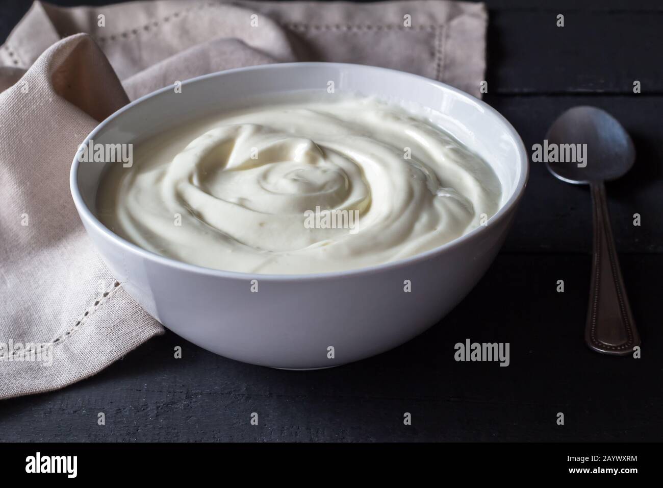 Yogurt greco in una ciotola bianca su un rustico tavolo di legno nero. Messa a fuoco selettiva Foto Stock