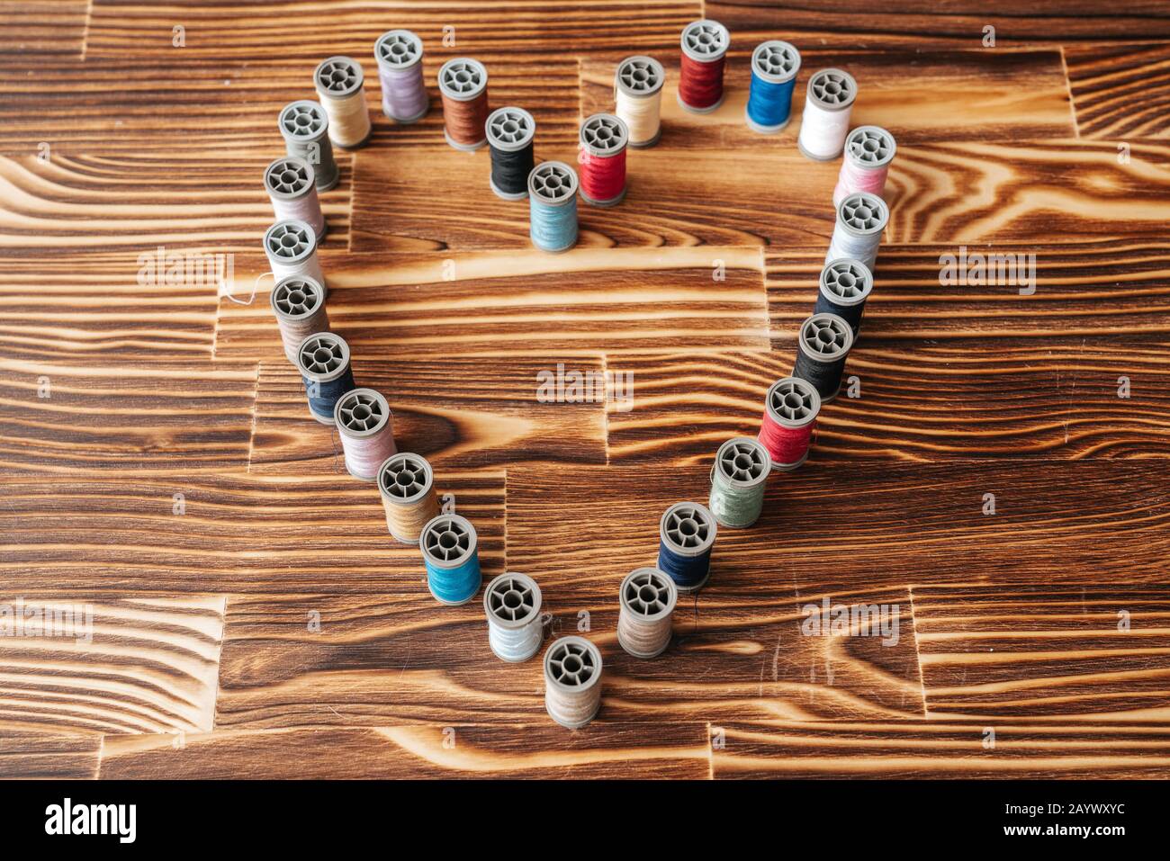 Molte bobine di filo di aline affiancate a forma di cuore su uno sfondo di legno Foto Stock
