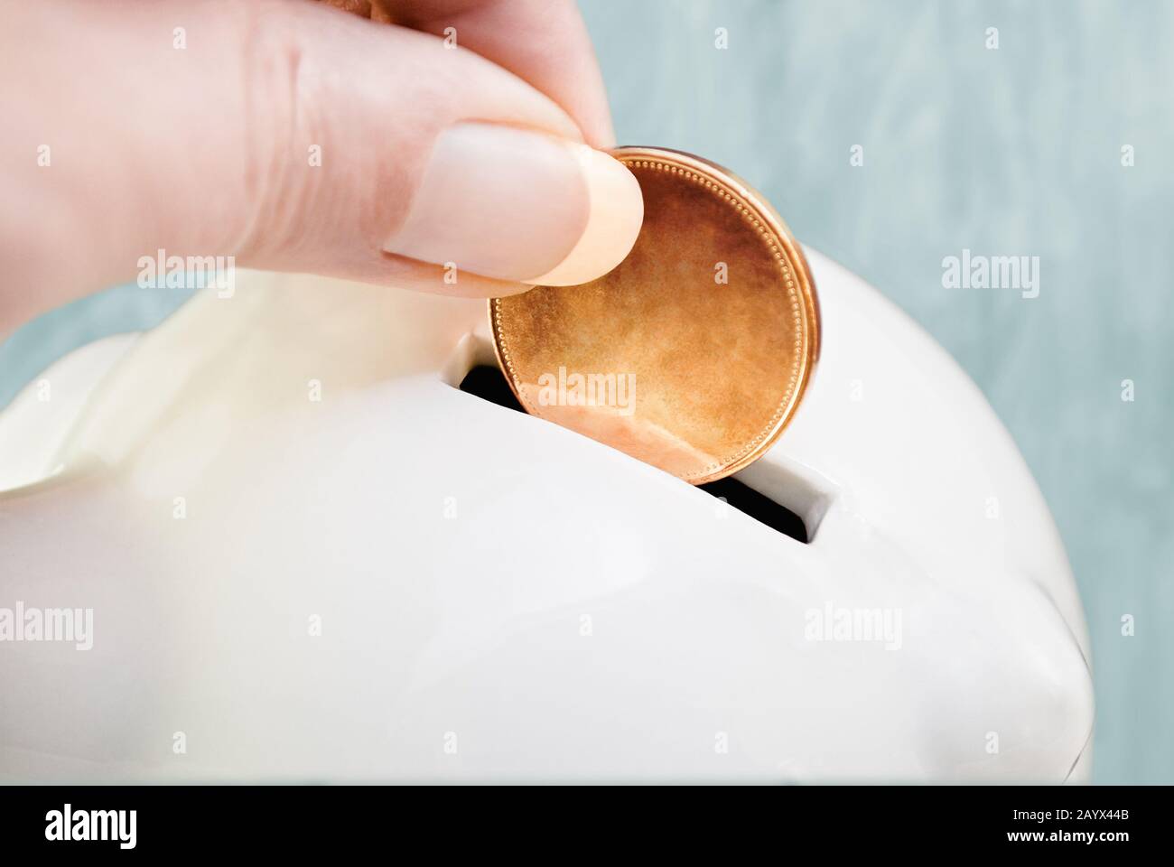 Una mano deposita una moneta vuota con valore ed emblema rimossi in una banca bianca piggy della cina. Sfondo azzurro. Foto Stock