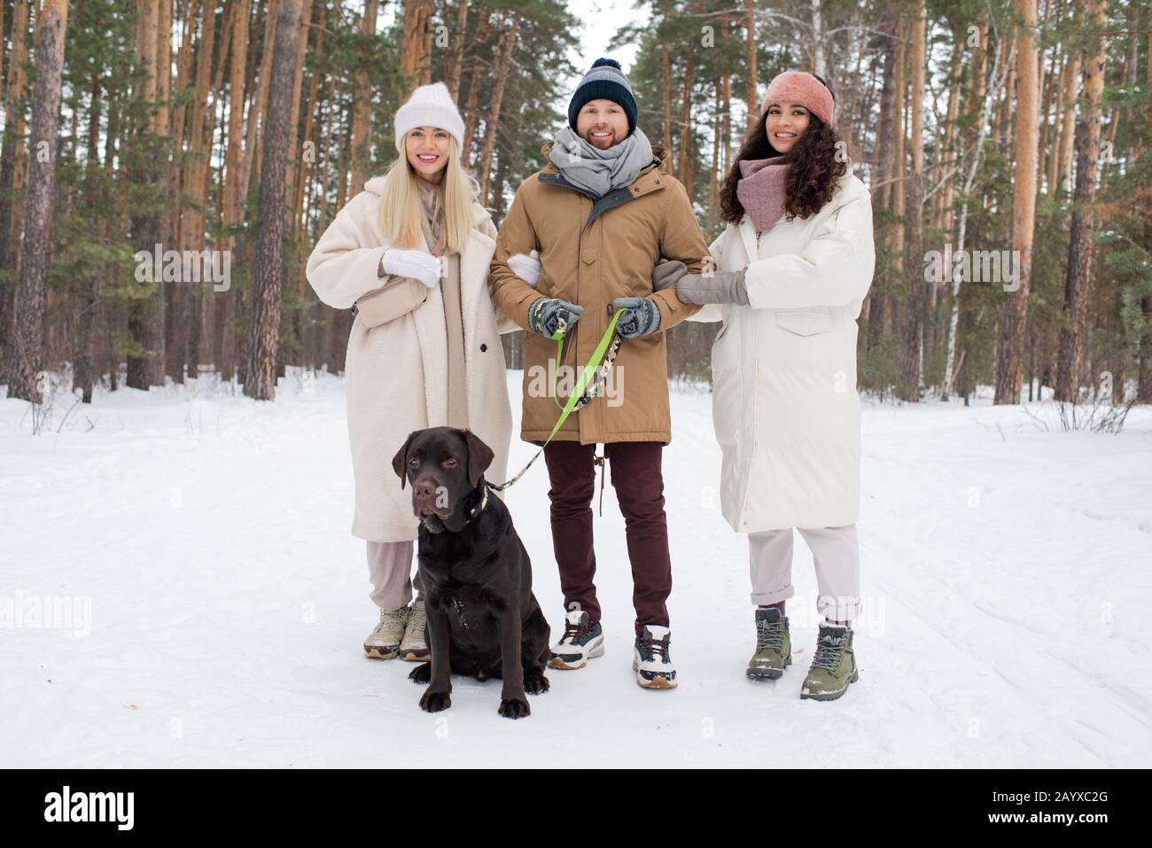 Foto orizzontale di gruppo intero di uomo caucasico e due belle donne che posano sulla macchina fotografica mentre camminano cane Foto Stock