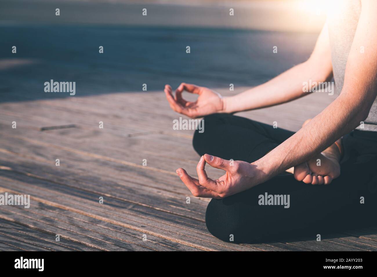 Dettaglio delle mani di un giovane che medita lo yoga praticando su alcune tavole di legno in posizione lotus. Foto Stock