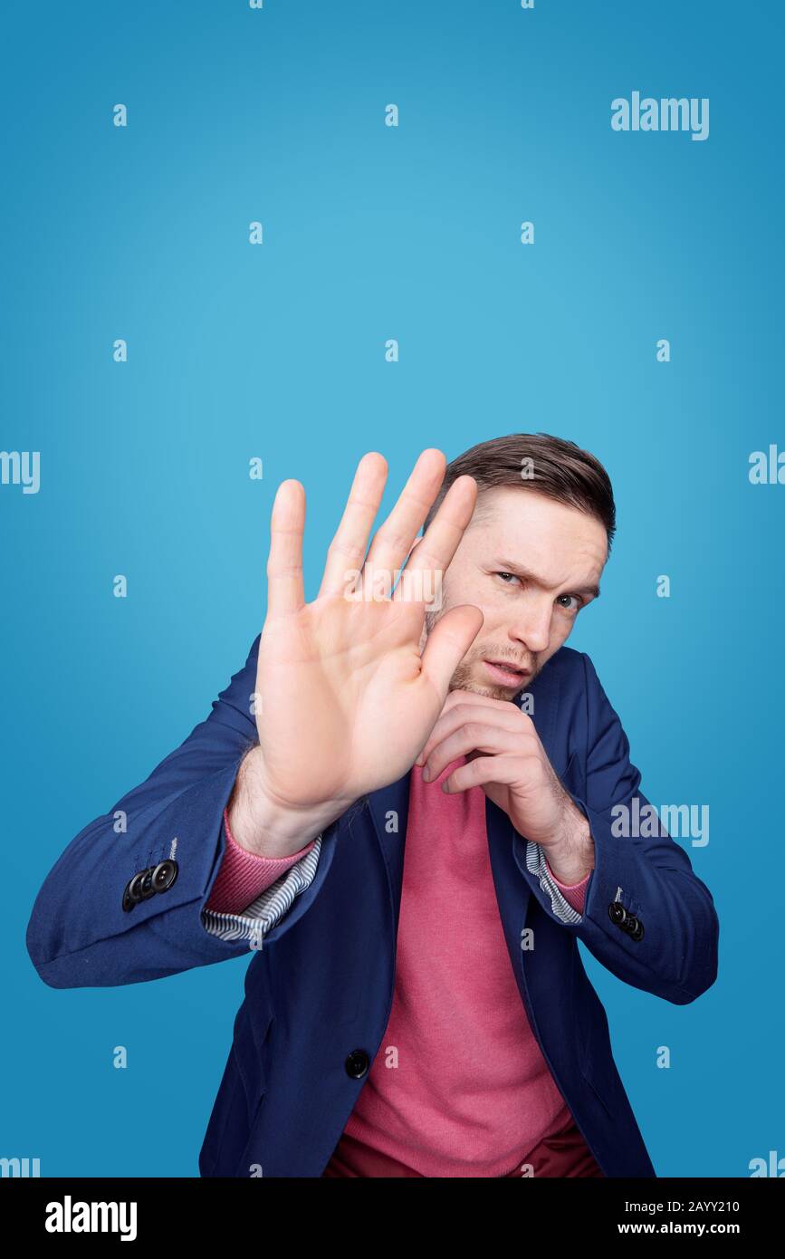 Ritratto di giovane uomo spaventato che accigliava la fronte e nasconde il viso dietro la mano contro sfondo blu Foto Stock