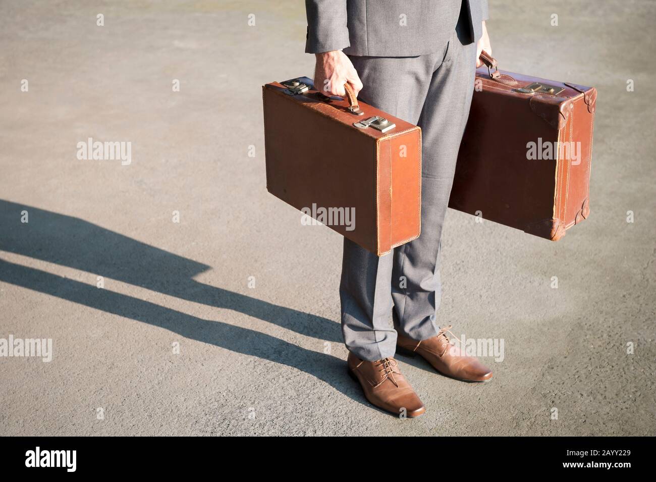 Uomo d'affari irriconoscibile che si trova all'aperto sulla strada in attesa con vecchie valigie marroni stagionato Foto Stock