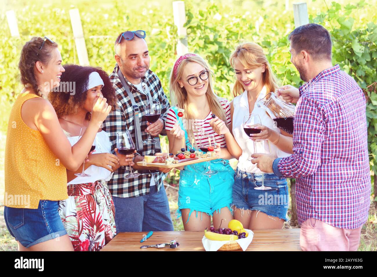 Giovani amici multietnici divertirsi all'aperto bere vino rosso all'aperto bar-b-que festa in campagna ristorante con giardino vigneto Foto Stock