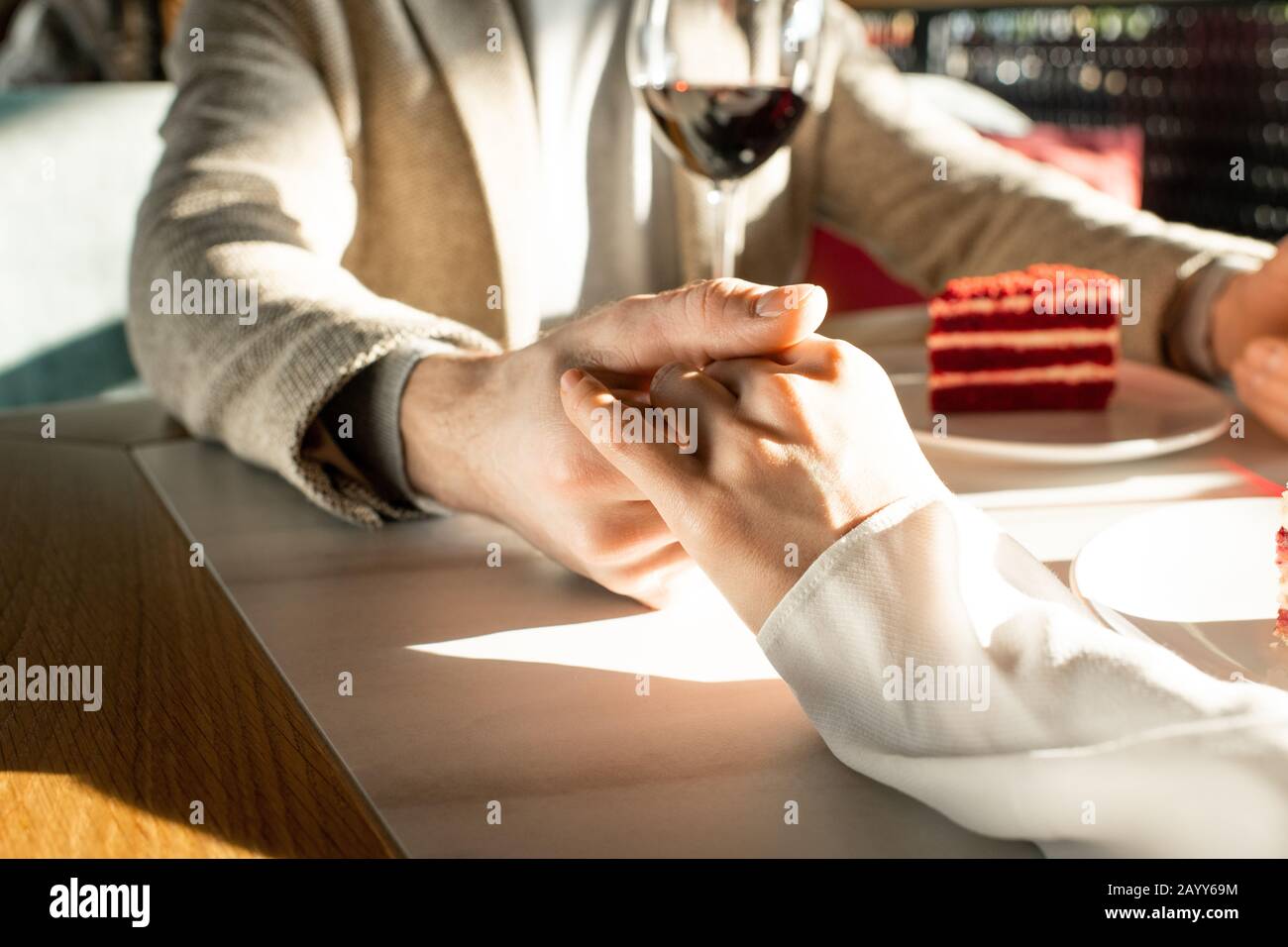 Uomo e donna irriconoscibili che amano passare il tempo in un ristorante moderno, delicatamente tenendo le mani, scatto orizzontale Foto Stock
