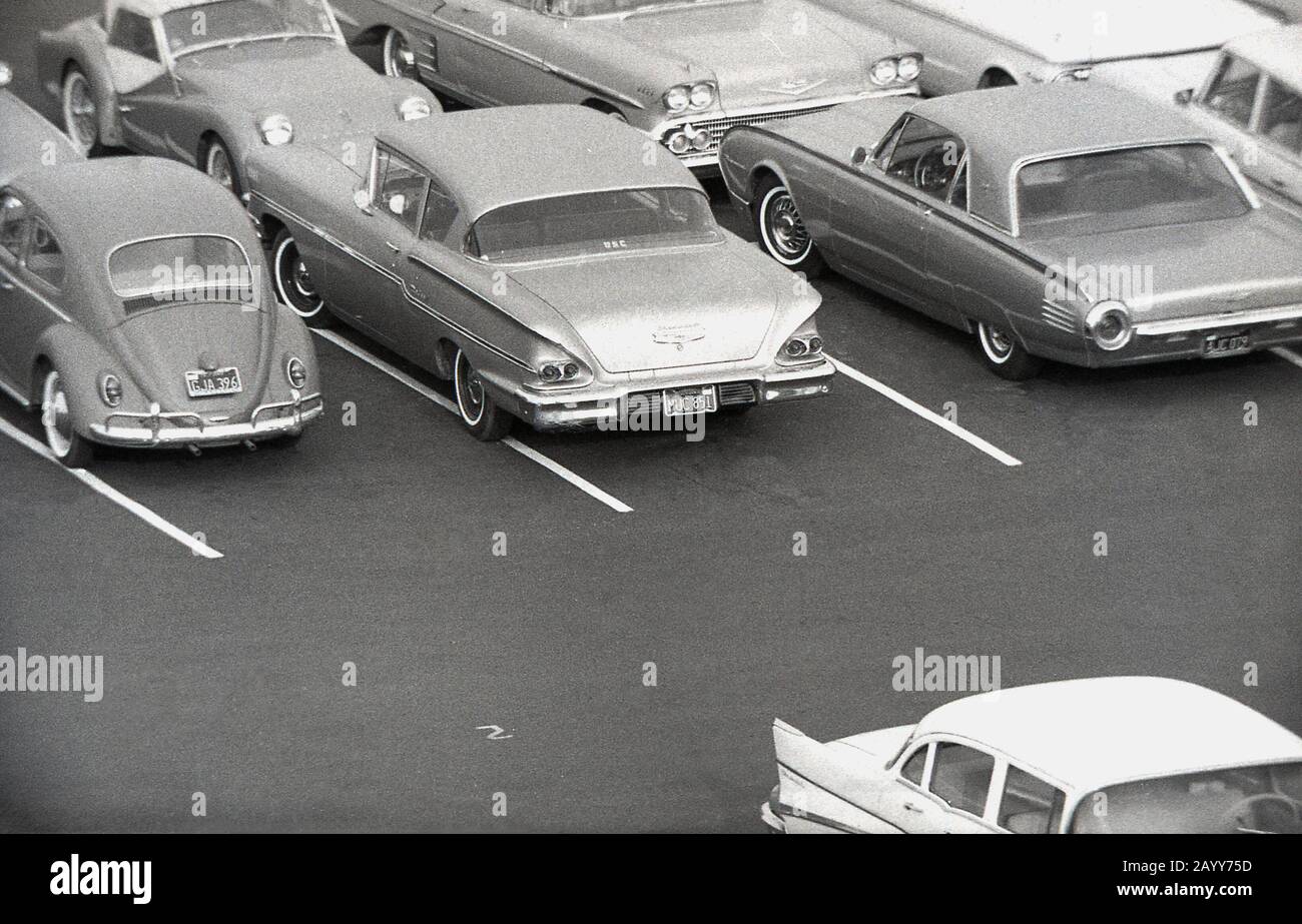 1964, storico, vista aerea di automobili americane dell'epoca parcheggiata in un parcheggio, California, USA, mostrando anche un Maggiolino Volkswagen. Foto Stock