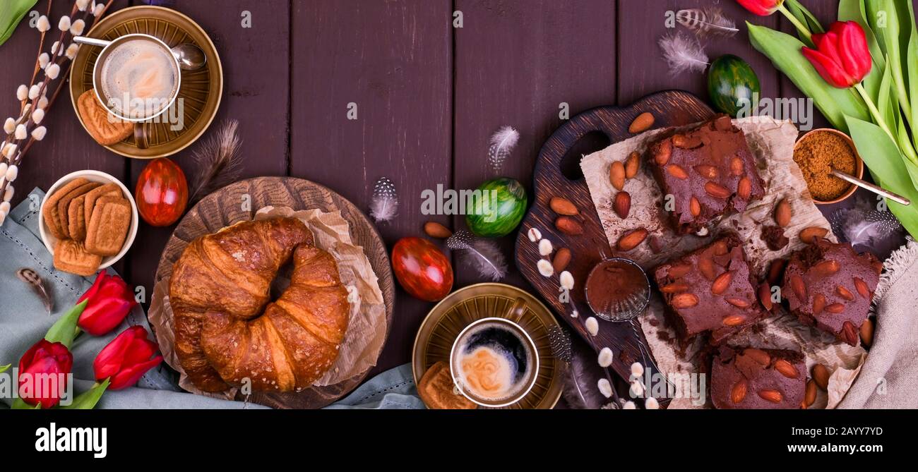 Colazione di Pasqua con caffè espresso fresco aromatico, croissant, torta brownie, uova colorate, tulipani rossi e salice. Caffè con dolci, fiori su un tavolo di legno. Vista dall'alto Foto Stock