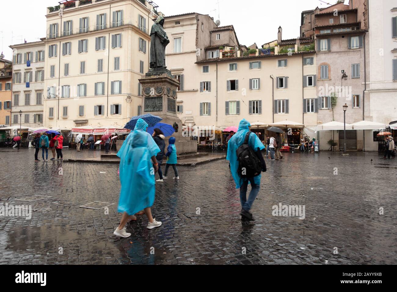 I turisti che camminano sotto la pioggia attraverso una piazza di ciottoli a Roma Italia Foto Stock