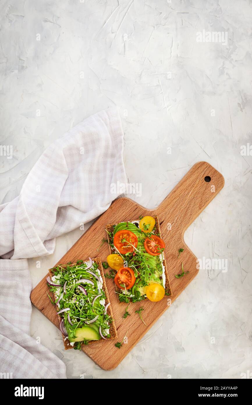 Toast di segale avocado con erbe verdi, cipolla e pomodori ciliegini, cibo sano Foto Stock