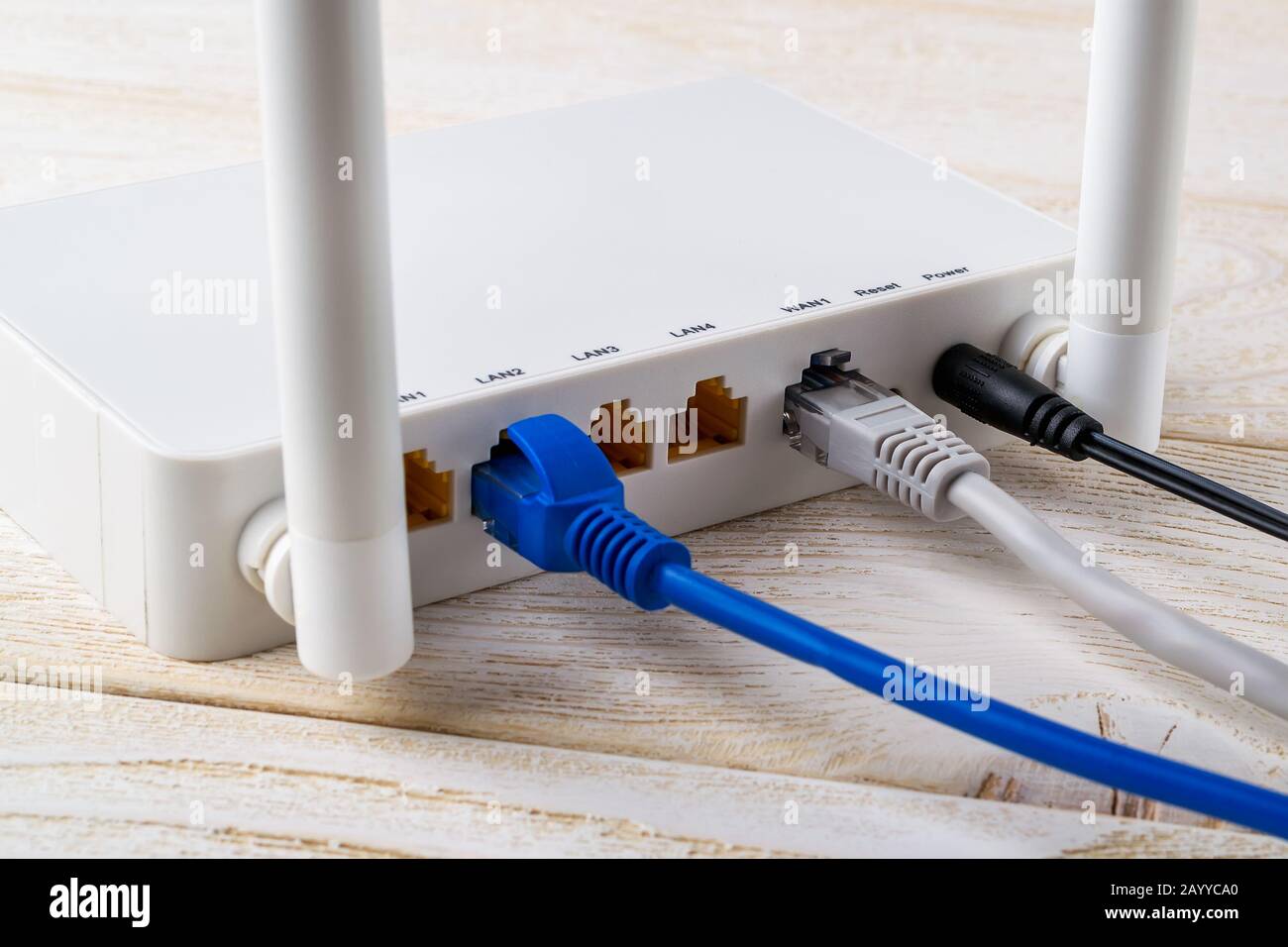 Primo piano dei cavi di rete collegati a un router wireless Wi-Fi bianco su un tavolo in legno bianco. Router WLAN con cavi Internet collegati a un tavolo Foto Stock