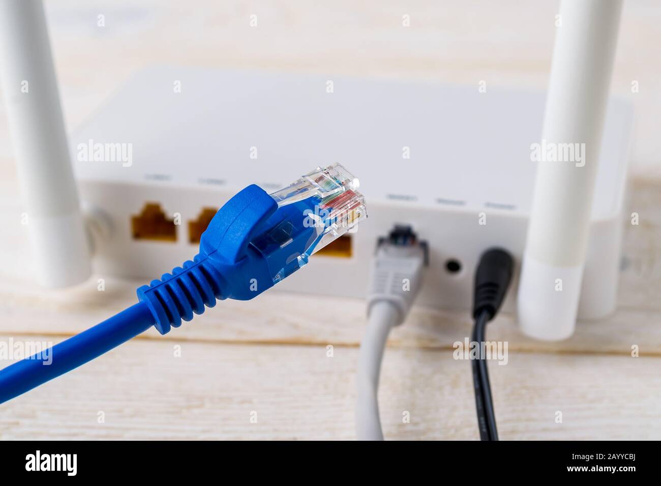 Primo piano del cavo di rete blu su uno sfondo di un router wireless Wi-Fi bianco su un tavolo di legno bianco. Router WLAN con cavi Internet collegati. Foto Stock