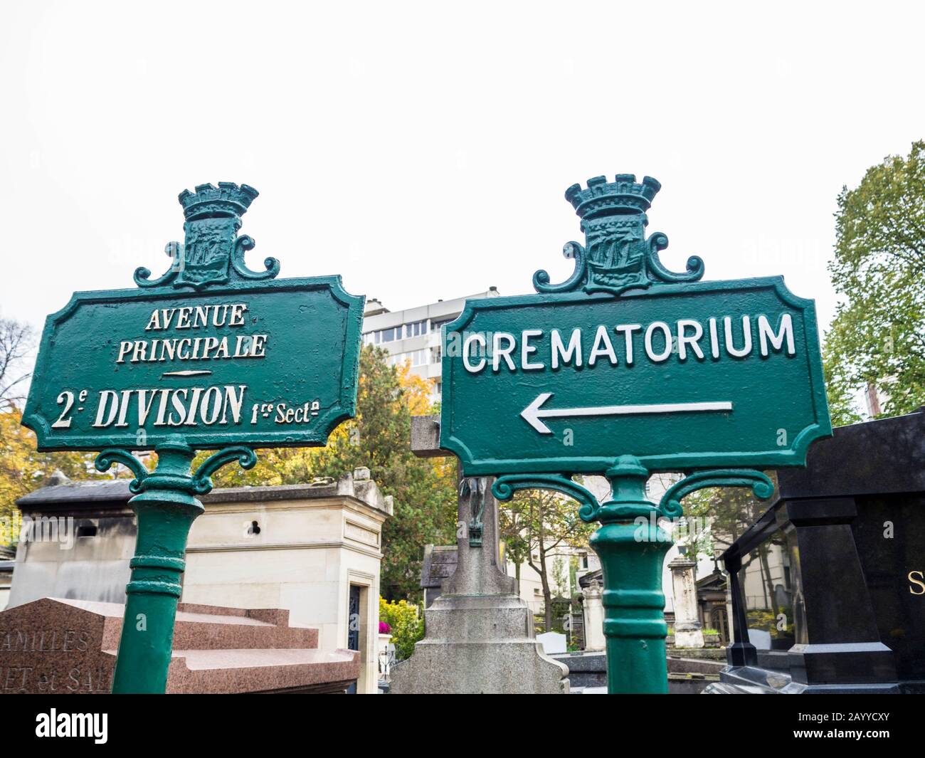 Vecchio segnale verde con il nome dei viali scritti in francese con bacground di alberi e monumenti funebri in un cimitero monumentale Foto Stock