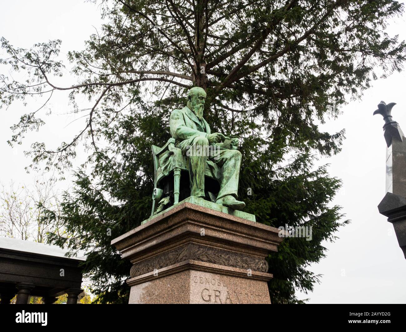 Antica statua di vecchi uomini seduti su una sedia in cima ad una vecchia tomba memoriale sotto l'albero in un cimitero monumentale Foto Stock