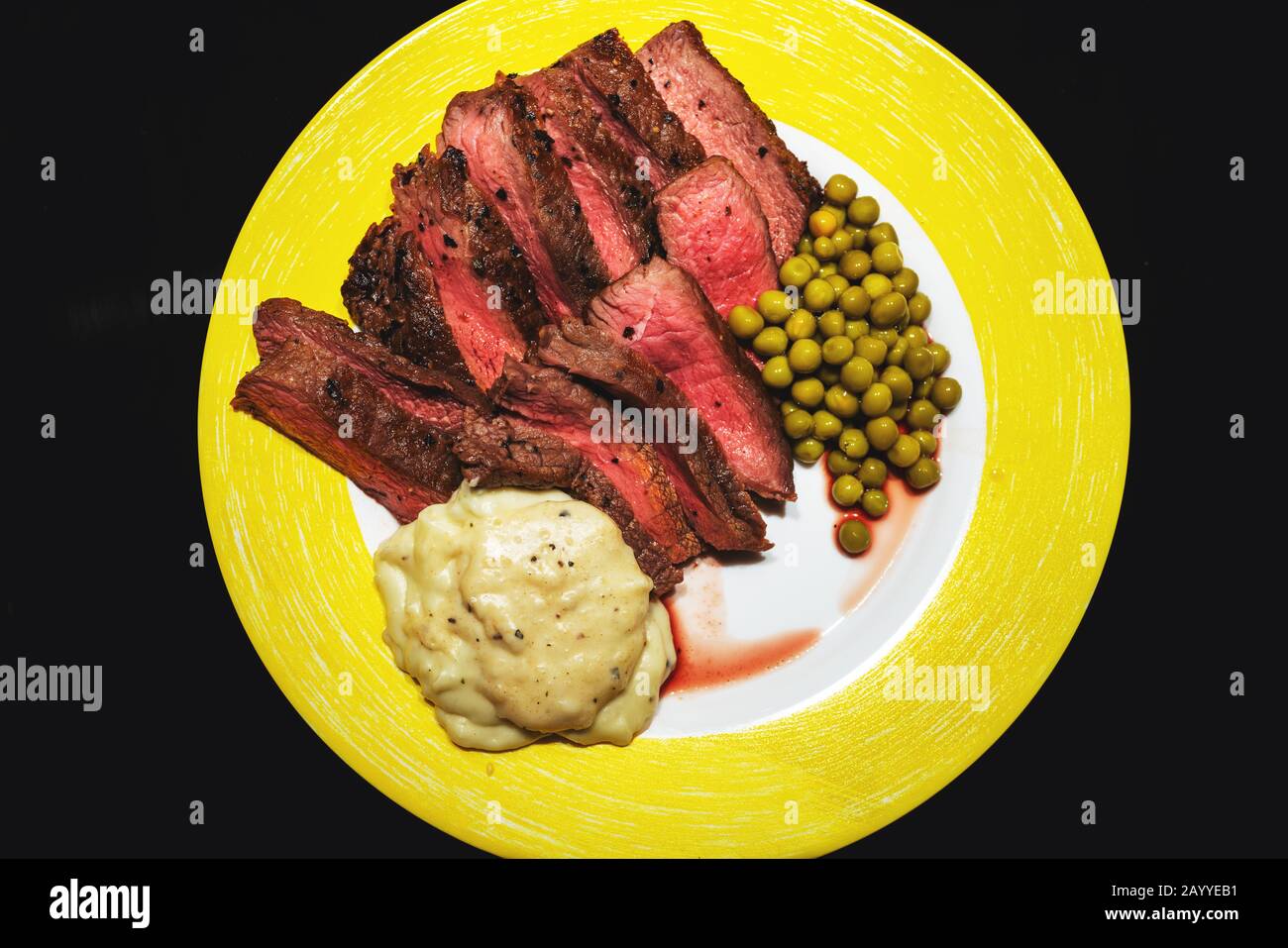 Bistecca fatta in casa di media-rara con piselli e salsa di panna su piatto giallo isolato su nero Foto Stock